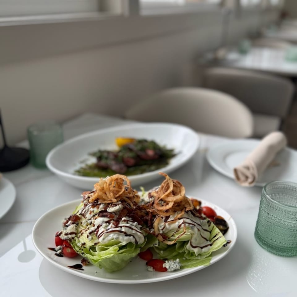 Plated wedge salads topped with creamy dressing, cherry tomatoes, blue cheese, balsamic drizzle, and crispy fried onions.